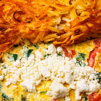 Close-up of hash browns and vegetable omelet with crumbled cheese.