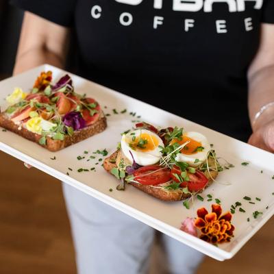 A waitperson holding a plate with an open sandwich on it.