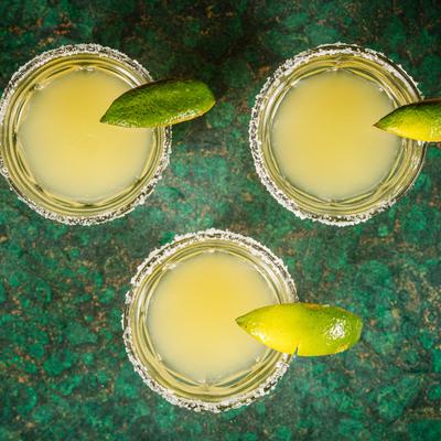 Three translucent yellow cocktails with lime, top view