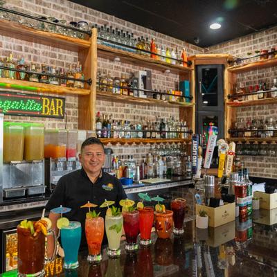 Bartender posing behind a bar adorned with vibrant Mexican-style cocktails.