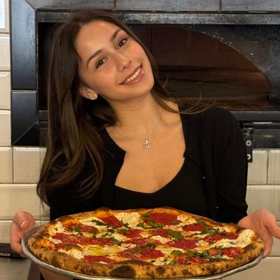 A staff member with a freshly baked margherita pizza.
