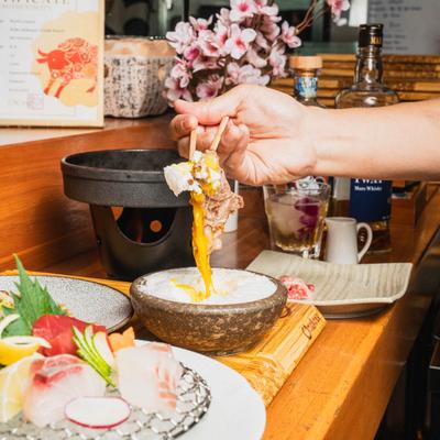 Hand taking food with chipsticks,  alongside sashimi and a bottle of whisky.