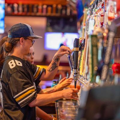 Bartender wearing a sports jersey pouring a beer from a tap at a bar.