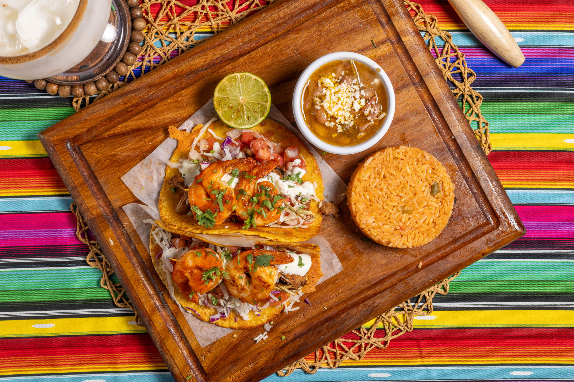 Shrimp tacos served with rice, beans, and lime on a wooden board