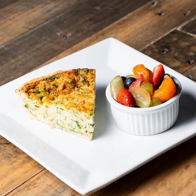 A slice of quiche with a side of mixed fruit.