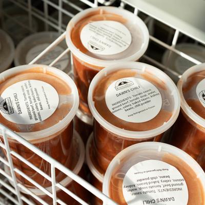 Plastic containers of chili stored in a wire freezer basket.