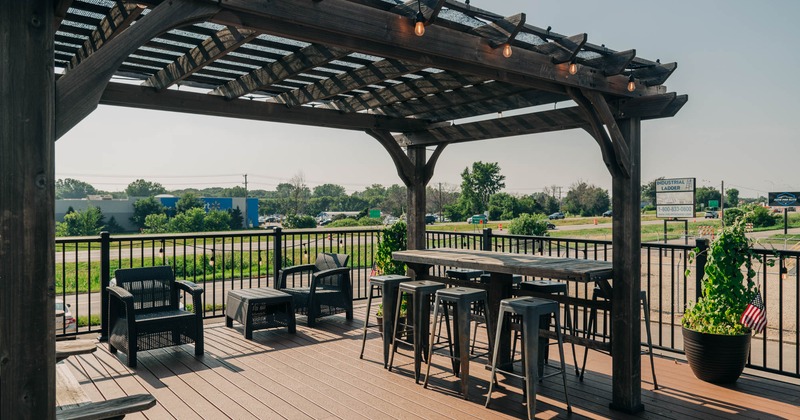 Outdoor patio with a pergola, bar table, stools, wicker chairs.