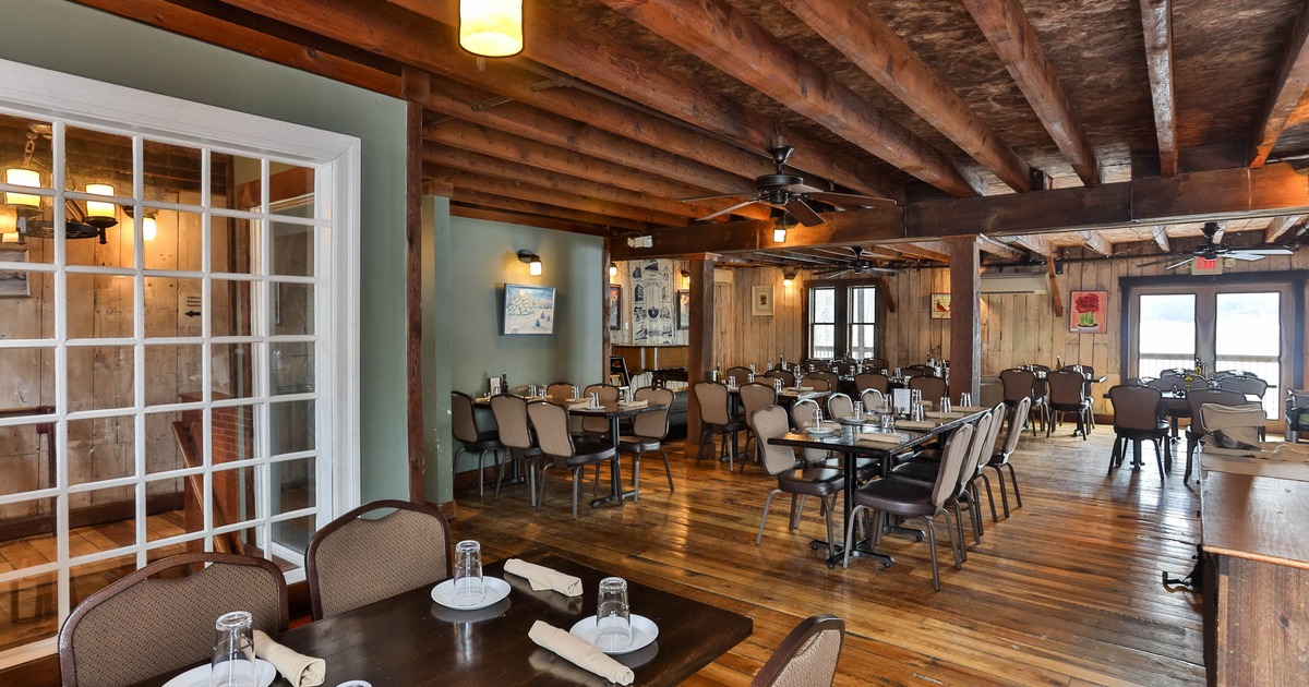 Rustic restaurant dining area with wooden floors and ceilings, set tables, and cushioned chairs