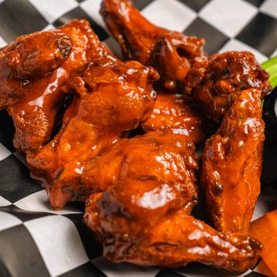 Chicken wings coated in sauce on checkered paper.
