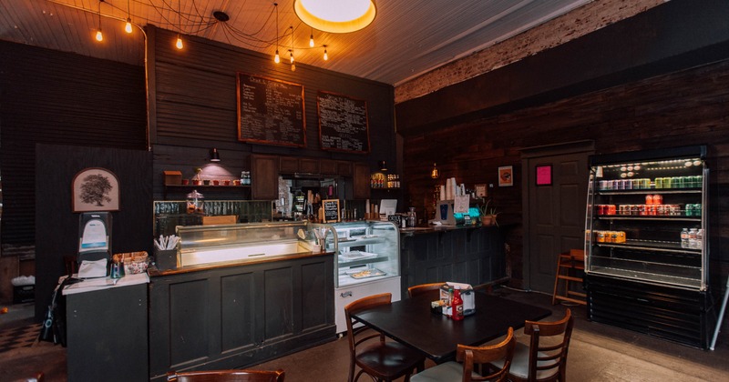 The interior of a warmly lit cafe with a service counter, menu board and seating area.