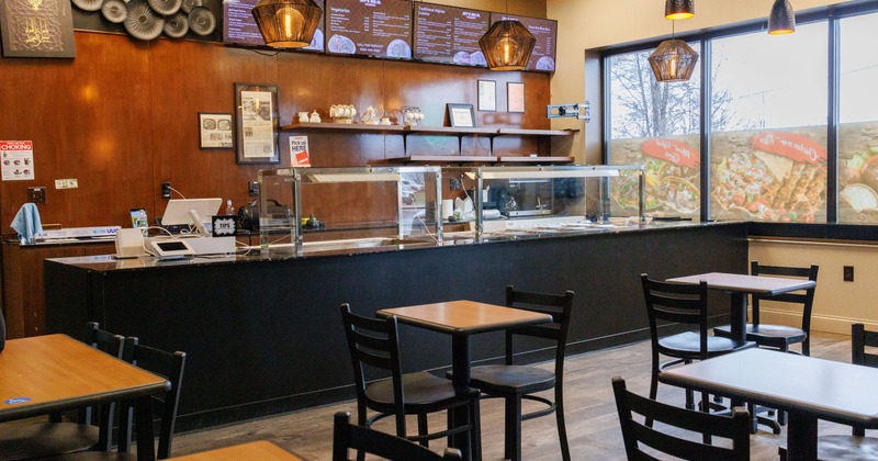Restaurant interior with wooden tables and chairs, food counter and a large windows.