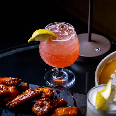 Victory Punch served in a clear stemmed glass alongside a plate of wings.