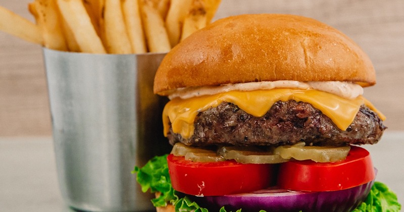 A cheeseburger with pickles, tomato, red onion, and lettuce, served with fries