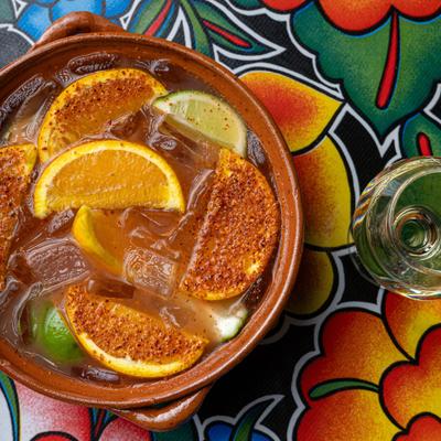 Mexican Cazuela cocktail garnished with seasoned citrus slices, served in a terracotta clay bowl.