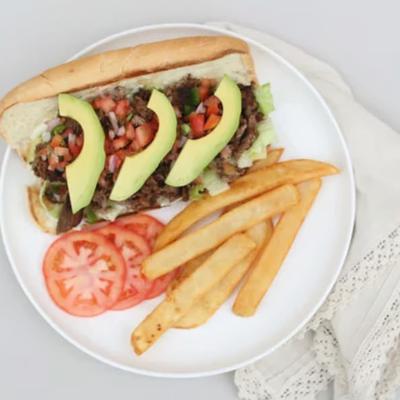 Loaded sandwich topped with fresh avocado and crispy fries on the side, top view.