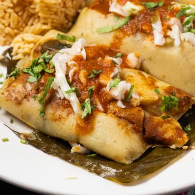 Tamales served on banana leaf with red salsa, shredded cabbage, and Mexican rice.