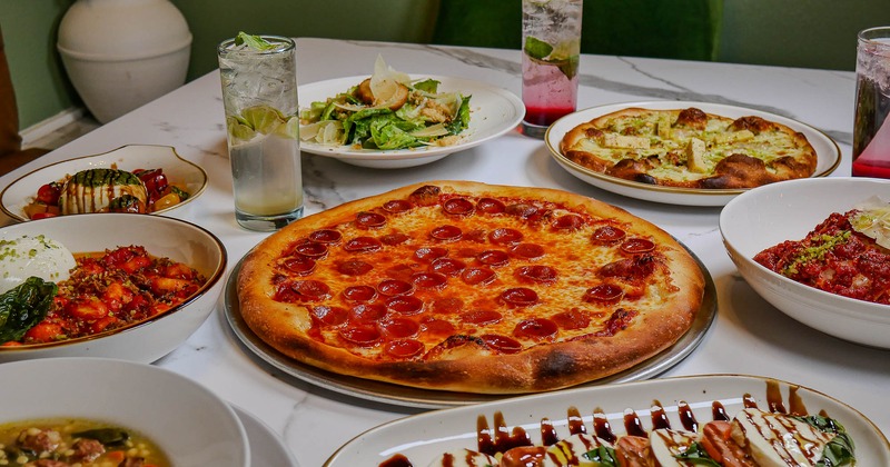 Pepperoni pizza surrounded by various food plates and drinks on the table