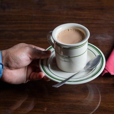 A person holds a saucer with a cup of Chai on it over a wooden table.