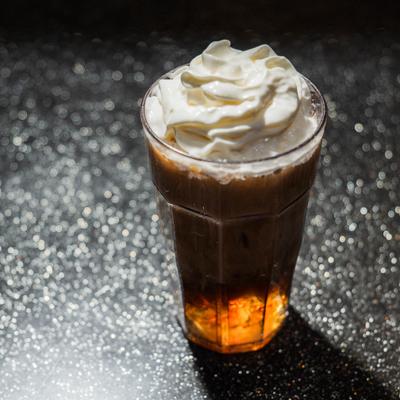 Iced drink in a tall glass topped with whipped cream.