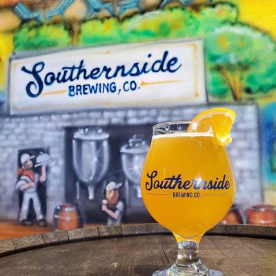 A glass of IPA on a barrel table with brewery mural art in the background