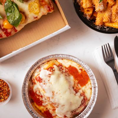 Baked ziti served with pizza and red pepper flakes.