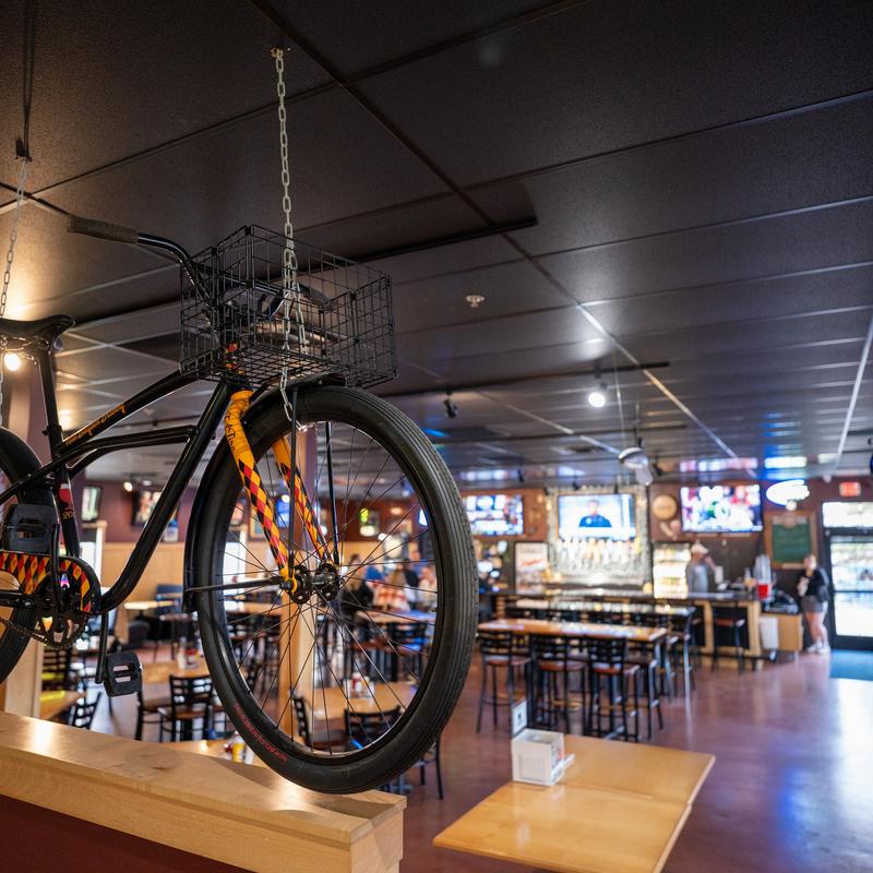 Bicycle suspended from the ceiling in a casual dining restaurant with tables, chairs, and TV screens in the background