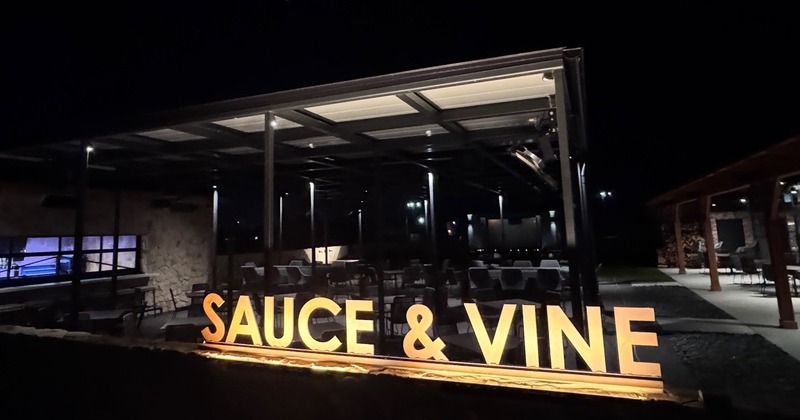 Nighttime view of patio seating and glowing Sauce & Vine sign