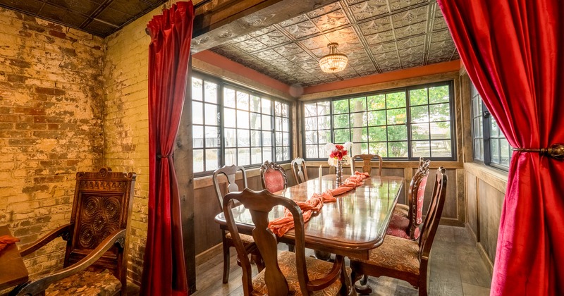 A vintage-style interior - a wooden table, ornate chairs, red velvet curtains and large windows