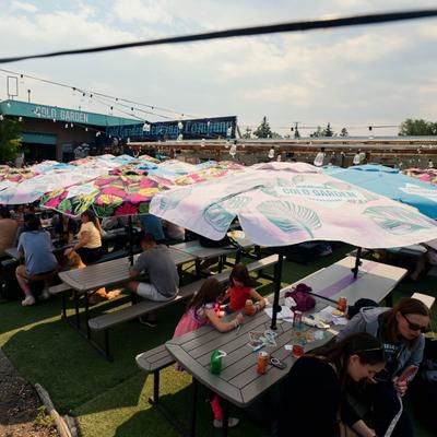 Guests enjoying drinks at picnic tables under vibrant umbrellas in Cold Garden’s beer garden.
