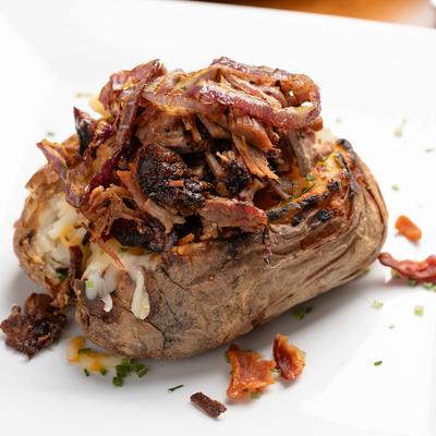 Baked potato, topped with pulled pork, butter, sour cream, bacon, and chives.