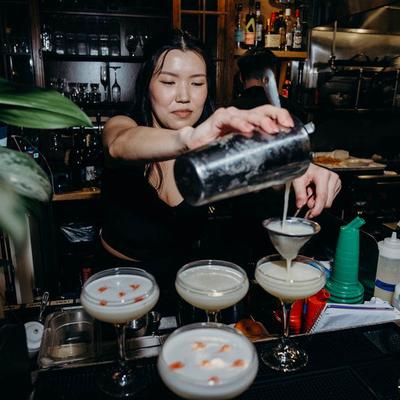 A bartender skillfully pouring cocktails into coupe glasses.