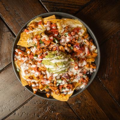Overhead view of a plate with loaded nachos on a rustic wooden table.