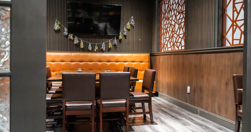 Dining area with orange leather banquette, brown chairs and wall-mounted TV