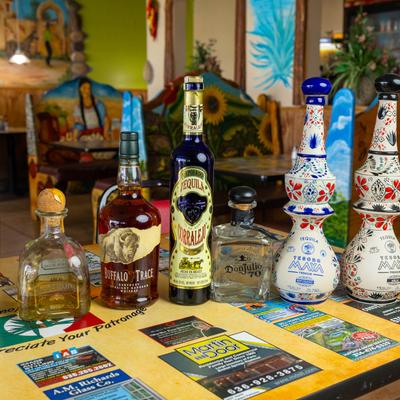 A collection of tequila and whiskey bottles on a table in a colorful dining area.