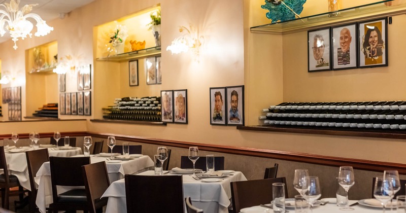 Interior, dining area, white cloth tables for four, ready for guests, stacked wine bottles