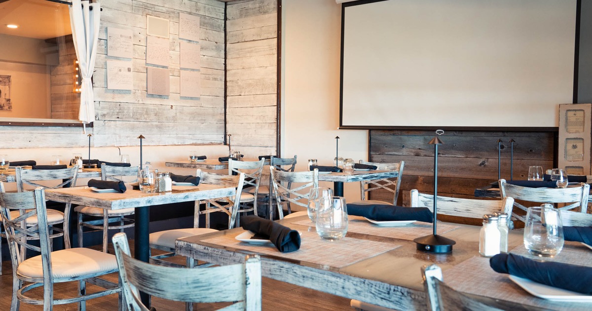 Tables with table settings and chairs arranged in front of a projection screen