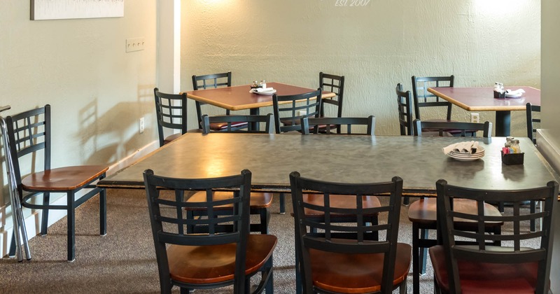 Interior dining area with tables and chairs, light green walls, and wall-mounted lights