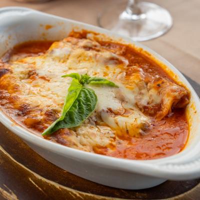 Lasagna served in a white oval baking dish, topped with melted cheese and basil.