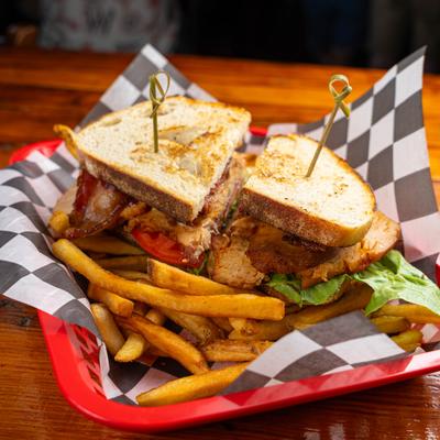 A sliced club sandwich with fries on checkered paper in a tray.