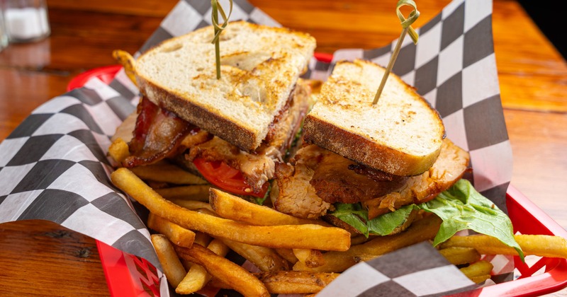 A sliced club sandwich with fries on checkered paper in a tray