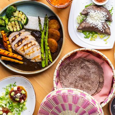 Table spread with grilled duck breast, vegetables, blue corn tortillas, and blue corn empanadas.