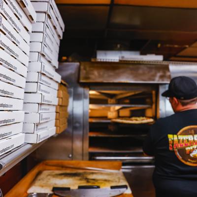 A staff member putting pizza in the oven.