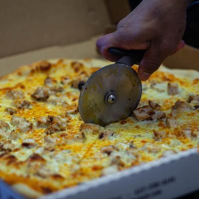 A person cutting a chicken pizza with a cutter.