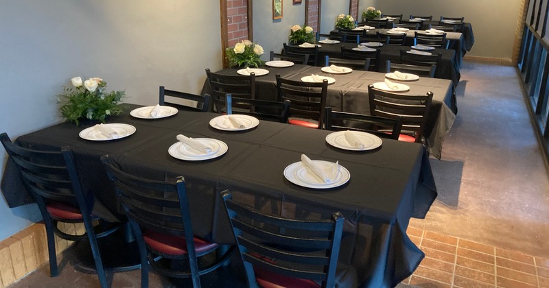 A dining area set up for an event, with multiple tables, each set with plates and napkins