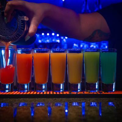 A row of assorted colorful shots with a hand pouring one.