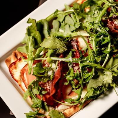 Margherita flatbread topped with arugula and grated cheese, close-up.