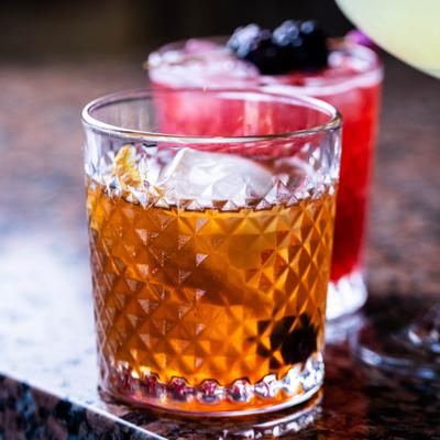 Two cocktails on a granite countertop, amber and red.