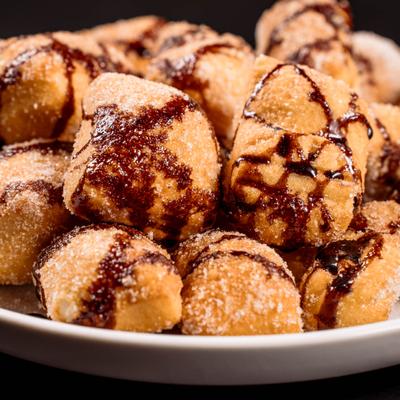 Zeppole with powdered sugar and chocolate drizzle.