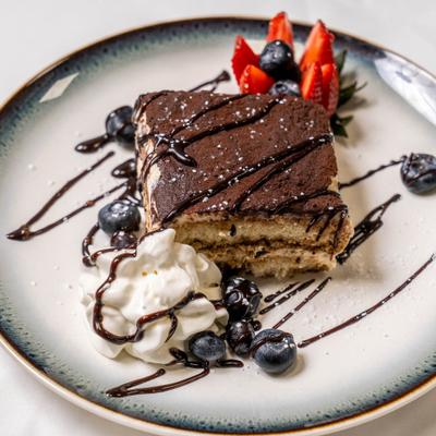Tiramisu dessert with chocolate drizzle, whipped cream, blueberries and strawberries.