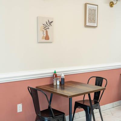 A wooden table with two black chairs against a pink and white wall with framed art.